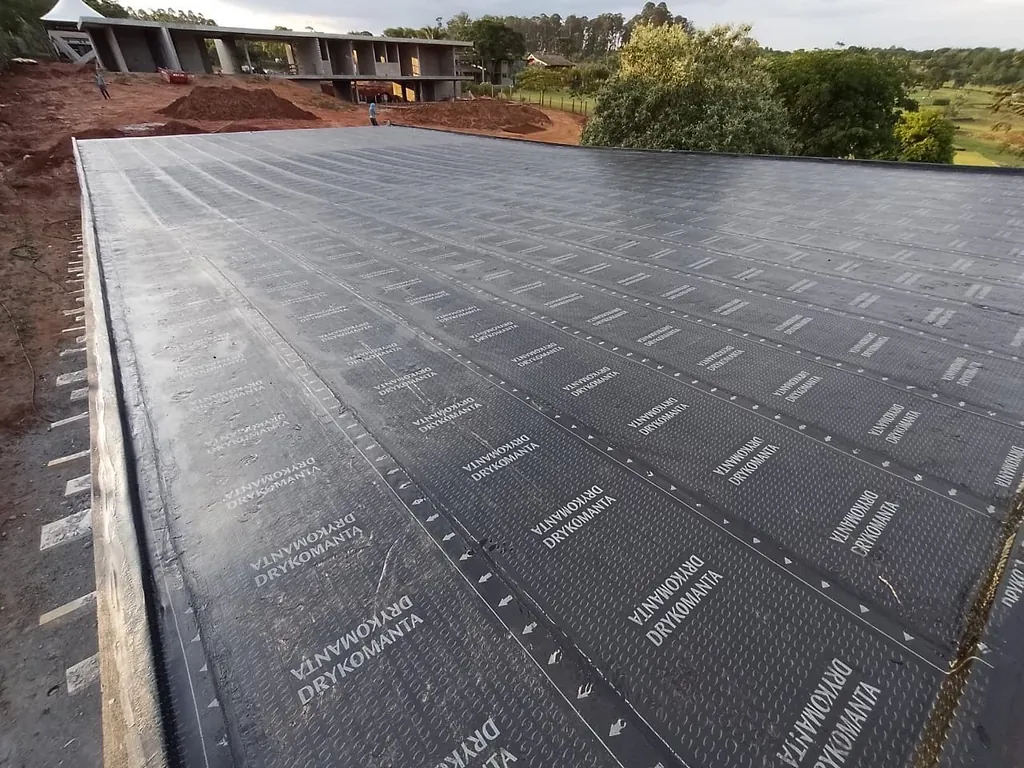 Laje grande com manta asfáltica preta aplicada, em obra com campo ao fundo